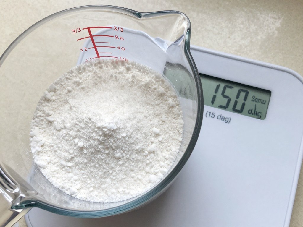 Trzy czwarte szklanki wypełnionej cukrem pudrem obok wagi pokazującej 15 dag